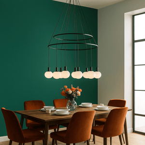 Dining room with a modern chandelier, wooden table, and orange chairs against a green wall.