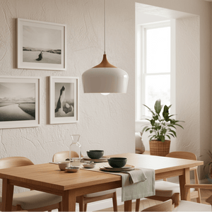 Scandinavian-style pendant light hanging above a wooden dining table set with dishes and a carafe, framed photos on the wall.