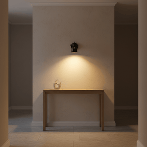 Indigo Mulberry wall lamp in matte black illuminating a wooden console table against a textured wall.
