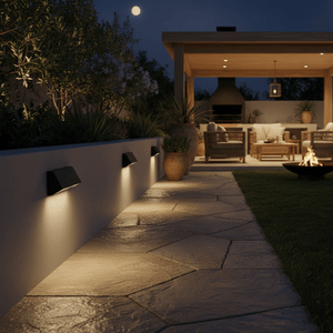 Outdoor scene featuring multiple black footlights illuminating a stone pathway beside a cozy patio.