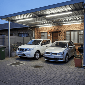 Two cars parked under a covered area illuminated by slim outdoor linear lights, enhancing visibility.