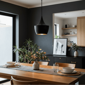 Black metal pendant light hanging above a wooden dining table with decorative plants and tableware.