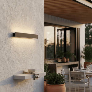 Linear wall light on a textured wall, casting warm light, with a small shelf holding a bowl and towel, patio behind