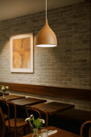 Wooden pendant light hanging in a restaurant setting with tables and chairs.
