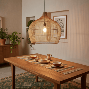Woven bamboo rattan pendant light hanging above a wooden dining table set with dishes and a pitcher.