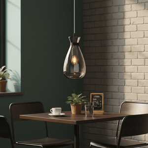 Smoke glass pendant light hanging above a wooden table with a coffee cup and plant.