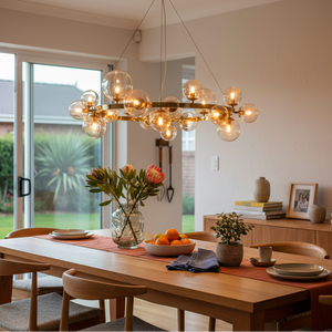Round bubble pendant light in French Gold with cognac glass above a dining table with flowers and fruit.