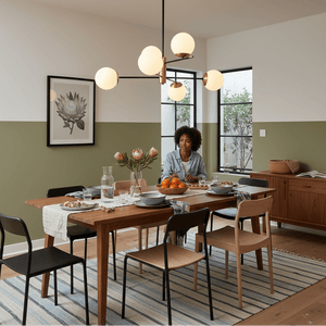 A modern dining room featuring a black and satin gold chandelier with opal glass shades, illuminating a wooden table set