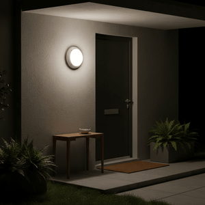 Outdoor wall light mounted beside a dark door, illuminating a small table and plants in a cozy entrance.