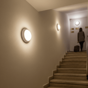 A person walking up stairs with Gelmi bulkhead lights mounted on the walls, providing illumination.