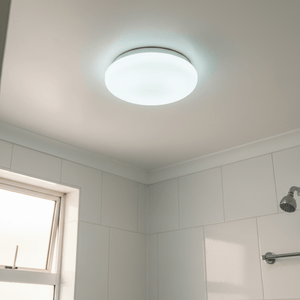 Ceiling-mounted white LED light in a modern bathroom setting, illuminating tiled walls.