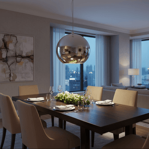 A large chrome pendant light hangs above a wooden dining table set with plates and glasses, surrounded by beige chairs.