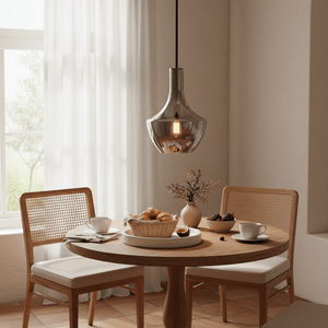 Smoke glass pendant light hanging over a round wooden dining table with woven chairs, croissants, coffee cups, and a vase