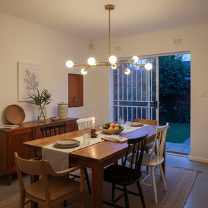 A modern dining area featuring a 9-light bronze pendant above a wooden table set with plates and a fruit bowl.