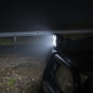 Close-up of a 50W LED work light mounted on a vehicle, illuminating a wet road at night.