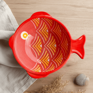 Top view of a red ceramic fish-shaped bowl with orange scale patterns, placed on a wooden surface.