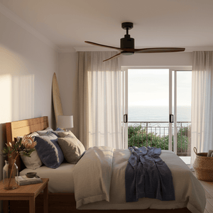 Modern ceiling fan with wood blades in a bright bedroom with ocean view and soft furnishings.