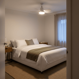 White ceiling fan with light on, mounted above a made bed in a bright bedroom