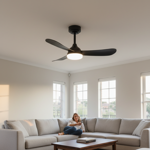 A black ceiling fan with integrated LED light hangs above a cozy living room with a woman relaxing on a sofa.