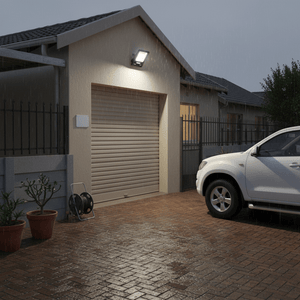 LED floodlight illuminating a driveway in the rain, mounted on a house wall, with a parked car nearby.