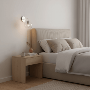 Satin silver wall light with glass globe above a cozy bed and wooden nightstand.