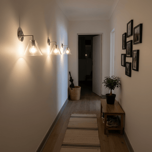 Three satin chrome wall lights with glass shades illuminating a stylish hallway with a wooden table and framed photos.