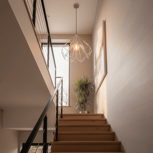 Chrome wire geometric pendant light with exposed bulb hanging above wooden stairs