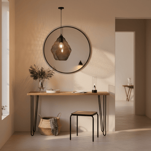 Black wire mesh pendant light hanging above a wooden console table with a round mirror and decorative items.