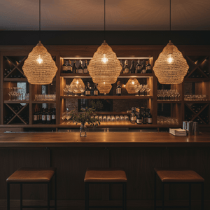 Three gold mesh pendant lights hanging above a wooden bar with wine bottles and glasses in the background.