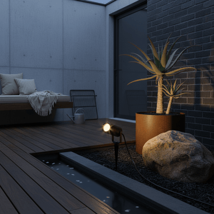 Garden spike light illuminating a potted plant on a wooden deck, with a rock and water feature nearby.