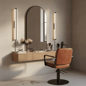 Modern vanity setup with a large mirror, lights, and a brown chair in a neutral-colored room.