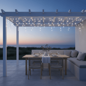 Twinkling icicle lights hang from a pergola above a dining table set for outdoor dining at sunset.