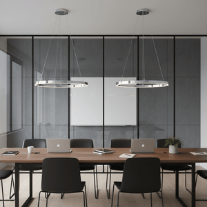 Two chrome hoop LED pendants hang above a modern conference table in a sleek office setting.