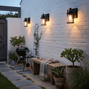 Outdoor patio area with a barbecue, bench, and wall-mounted lights on a white brick wall.