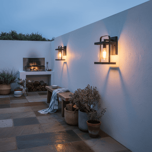 Two Cradock outdoor wall lights illuminate a cozy patio area with a fireplace and plants.