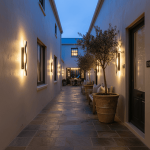 Outdoor scene featuring Bali Wave wall lights illuminating a stylish walkway with potted plants and seating.