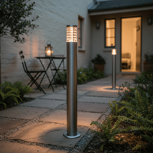 Stainless steel bollard lights illuminating a garden pathway with potted plants and a small outdoor seating area.