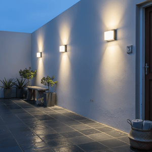 Outdoor LED wall lights mounted on a textured white wall, illuminating a patio area with plants and a wooden bench.