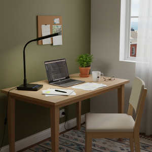A modern desk lamp with a goose neck positioned beside a laptop on a wooden desk, surrounded by stationery and a plant.