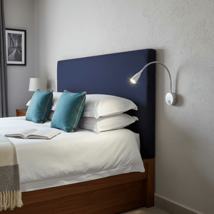 LED wall light mounted beside a bed, featuring a flexible goose neck and modern chrome finish, illuminating a book.