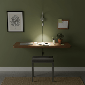 A modern workspace featuring a flexible goose neck LED wall light above a wooden desk with an open book, laptop, and potted