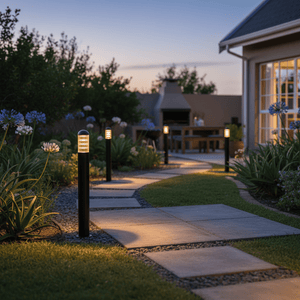Montague 1100 Bollard Light illuminating a garden pathway with flowers and a patio in the background.
