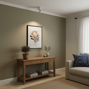 A modern white surface-mount downlight illuminating artwork above a wooden console table in a stylish living room.
