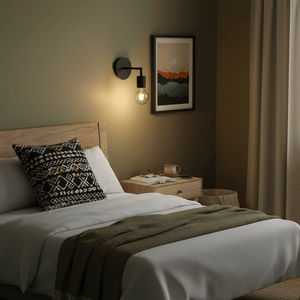 Black wall light mounted beside a bed, illuminating a cozy bedroom with a wooden headboard and decorative pillow.