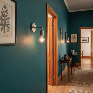 Satin chrome wall light illuminating a teal hallway, enhancing decor with a modern touch.