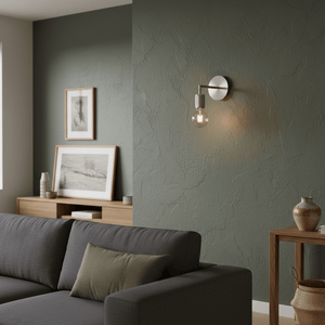 Satin chrome wall light mounted on a textured green wall, illuminating a cozy living space with a sofa and decor.