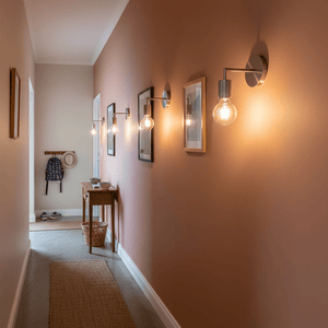 Satin chrome wall lights illuminating a stylish hallway with framed pictures and a console table.