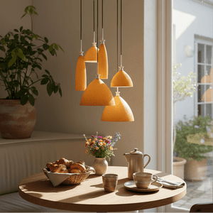 Six orange ribbed glass pendant shades hanging from black cords over a wooden dining table