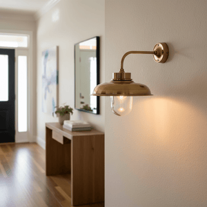 Antique brass wall lamp illuminating a hallway, with a wooden console table and mirror in the background.