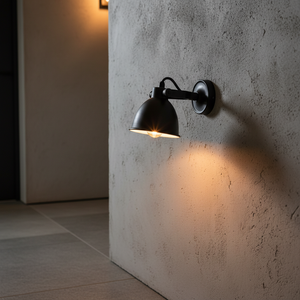 Maxim Cover wall lamp in matte black mounted on a textured wall, casting warm light below.